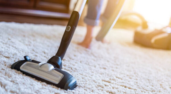 Young woman using a vacuum cleaner while cleaning carpet in the house.